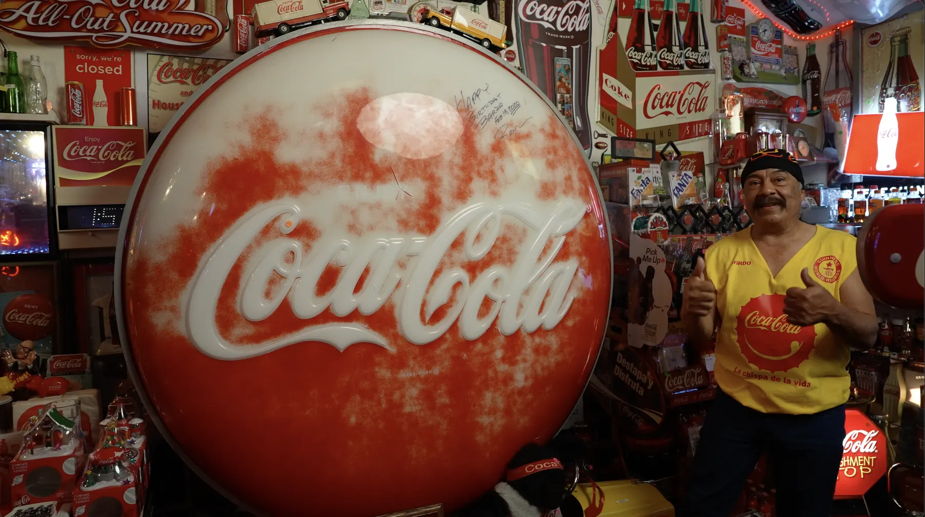 Bardo Cuellar giving a thumbs up next to the large light-up Coca-Cola button sign from his friend Ron, signed with a birthday message